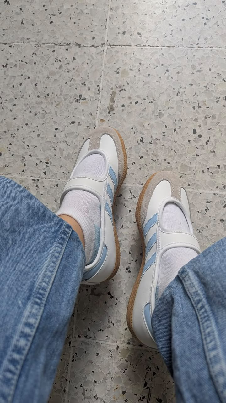 Adidas Samba Jane is available for delivery, delivery is Nat, feet, shoes, socks, jeans, Adidas, sneakers, white sneakers, blue stripes, light blue, denim, terrazzo floor, tiled floor, indoor, casual fashion, top-down view, high angle shot, personal perspective, comfortable, neutral colors, textured floor, everyday style, sportswear, modern aesthetic, footwear, lifestyle